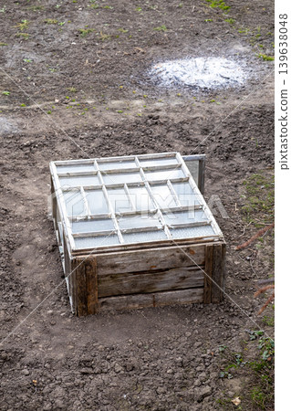 Rustic wooden cold frame box with glass window lid placed in soil, representing sustainable urban gardening, early spring seedling protection, and traditional small scale vegetable farming 139638048
