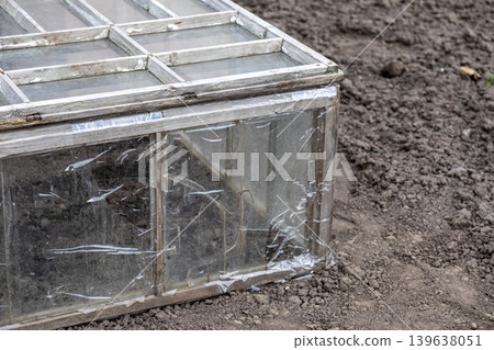 Rustic cold frame greenhouse made from reclaimed window panes, placed on garden soil for seasonal seedling protection, promoting sustainable urban agriculture and small scale vegetable farming Rustic cold frame greenhouse made from reclaimed window panes, placed on garden soil for seasonal seedling protection, promoting sustainable urban agriculture and small scale vegetable farming 139638051