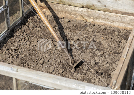 An old metal hoe rests in the soil of a wooden cold frame, illustrating gardening preparation and organic plant cultivation during the early spring season for small scale home farm projects An old metal hoe rests in the soil of a wooden cold frame, illustrating gardening preparation and organic plant cultivation during the early spring season for small scale home farm projects 139638113