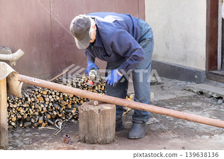 An elderly man uses an electric angle grinder to cut a metal pipe outdoors, representing home improvement projects, professional maintenance skills, and DIY construction tasks in a sunny yard An elderly man uses an electric angle grinder to cut a metal pipe outdoors, representing home improvement projects, professional maintenance skills, and DIY construction tasks in a sunny yard 139638136