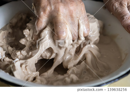 Elderly person hand mixing organic yeast starter in a ceramic bowl for bread baking, representing traditional homemade cooking, slow food culture, and authentic culinary technique Elderly person hand mixing organic yeast starter in a ceramic bowl for bread baking, representing traditional homemade cooking, slow food culture, and authentic culinary technique 139638256
