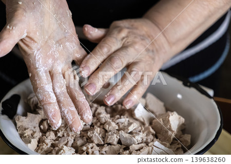 Elderly person crumbling fresh yeast in a bowl for baking bread, emphasizing traditional culinary preparation methods and the craft of homemade artisan food production at home Elderly person crumbling fresh yeast in a bowl for baking bread, emphasizing traditional culinary preparation methods and the craft of homemade artisan food production at home 139638260