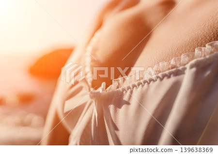Lingerie woman beach close up of young female wearing white lace top on a sunny pebble coast during golden hour Lingerie woman beach close up of young female wearing white lace top on a sunny pebble coast during golden hour 139638369