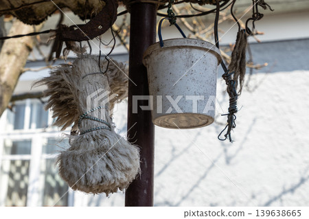 Old plastic bucket and tied rope hanging on a garden pole, depicting rural life, rustic maintenance, or outdoor organization in a weathered backyard setting during daytime 139638665