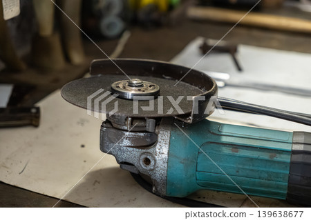 Angle grinder with abrasive cutting disc on a workbench, professional power tool for metal fabrication, construction site maintenance and industrial repair tasks in a workshop Angle grinder with abrasive cutting disc on a workbench, professional power tool for metal fabrication, construction site maintenance and industrial repair tasks in a workshop 139638677