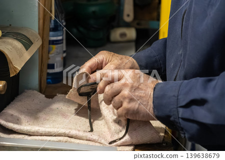 An elderly optician carefully cleans black eyeglasses with a soft cloth in his workshop, emphasizing precision maintenance, eyewear care, and professional optical service quality An elderly optician carefully cleans black eyeglasses with a soft cloth in his workshop, emphasizing precision maintenance, eyewear care, and professional optical service quality 139638679