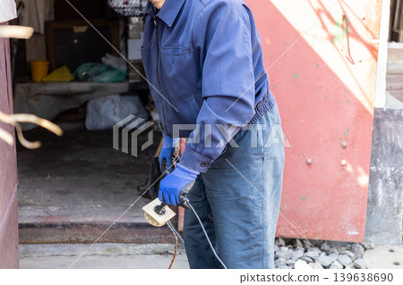Manual worker in uniform holding old electrical plug outside garage, illustrating maintenance tasks, technical repair services, utility work, professional craftsmanship and labor Manual worker in uniform holding old electrical plug outside garage, illustrating maintenance tasks, technical repair services, utility work, professional craftsmanship and labor 139638690