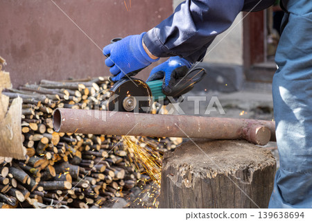 A professional construction worker uses a powerful electric angle grinder to cut through a metal pipe while bright sparks fly across the outdoor workshop during an industrial task A professional construction worker uses a powerful electric angle grinder to cut through a metal pipe while bright sparks fly across the outdoor workshop during an industrial task 139638694