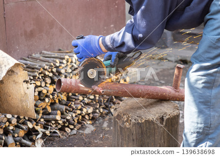 Industrial worker using an electric angle grinder to cut a metal pipe, generating bright orange sparks while performing heavy construction or mechanical maintenance work outdoors Industrial worker using an electric angle grinder to cut a metal pipe, generating bright orange sparks while performing heavy construction or mechanical maintenance work outdoors 139638698
