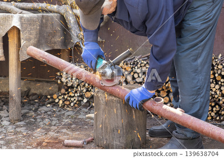 Craftsman using an angle grinder to cut a metal pipe in a backyard, emphasizing heavy industry work, precise manual labor, home improvement, and professional maintenance tasks Craftsman using an angle grinder to cut a metal pipe in a backyard, emphasizing heavy industry work, precise manual labor, home improvement, and professional maintenance tasks 139638704