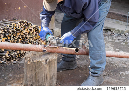 Metalworker using an angle grinder to cut a rusted pipe outdoors, highlighting manual labor, professional construction maintenance, industrial repair tasks, and craftsmanship skills Metalworker using an angle grinder to cut a rusted pipe outdoors, highlighting manual labor, professional construction maintenance, industrial repair tasks, and craftsmanship skills 139638713