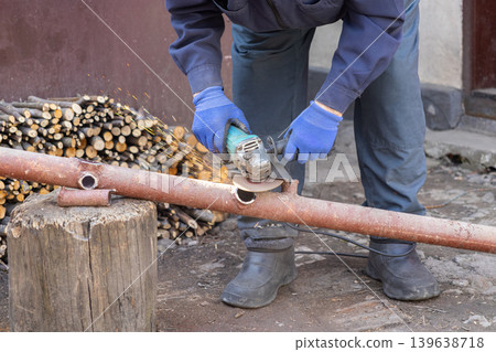 A professional construction worker uses a powerful angle grinder to cut a metal pipe, showcasing industrial craftsmanship and skilled metalworking techniques on a busy work site A professional construction worker uses a powerful angle grinder to cut a metal pipe, showcasing industrial craftsmanship and skilled metalworking techniques on a busy work site 139638718