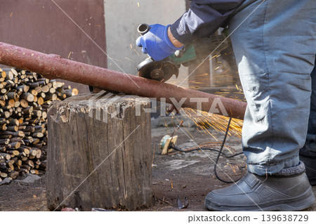 A dedicated worker uses an electric angle grinder to cut a metal pipe, creating bright sparks in an outdoor workshop while demonstrating professional industrial craftsmanship and home renovation 139638729