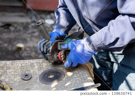 A construction worker uses an electric handheld grinder with a wire brush attachment to clean metal surfaces, showcasing professional industrial repair and essential skilled craft labor tasks A construction worker uses an electric handheld grinder with a wire brush attachment to clean metal surfaces, showcasing professional industrial repair and essential skilled craft labor tasks 139638741