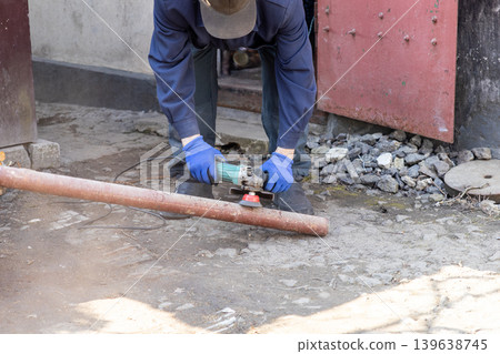 A professional manual worker uses a powerful electric angle grinder to smooth a rusty metal pipe, showcasing industrial repair, construction site maintenance, and precise metalworking craft A professional manual worker uses a powerful electric angle grinder to smooth a rusty metal pipe, showcasing industrial repair, construction site maintenance, and precise metalworking craft 139638745