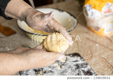 Elderly hands shaping dough for cottage cheese syrniki, preparing traditional homemade breakfast in a rustic kitchen setting, emphasizing culinary heritage, artisan craft, and authentic food 139639032