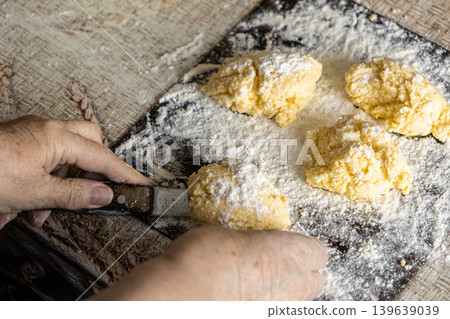Elderly person shaping fresh homemade syrniki cottage cheese pancakes on a floured wooden board, highlighting traditional culinary skills and the authentic atmosphere of home cooking process Elderly person shaping fresh homemade syrniki cottage cheese pancakes on a floured wooden board, highlighting traditional culinary skills and the authentic atmosphere of home cooking process 139639039