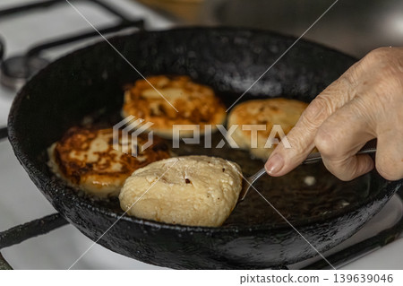 Senior person frying cottage cheese syrniki in a rustic cast iron skillet, focusing on homemade traditional breakfast preparation and culinary skills in a bright home kitchen environment setting Senior person frying cottage cheese syrniki in a rustic cast iron skillet, focusing on homemade traditional breakfast preparation and culinary skills in a bright home kitchen environment setting 139639046
