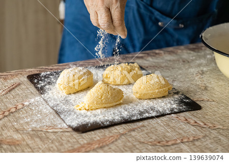 A chef dusts fresh cottage cheese syrniki with flour on a wooden board to highlight traditional culinary craft during the preparation of wholesome homemade breakfast food in a rustic kitchen A chef dusts fresh cottage cheese syrniki with flour on a wooden board to highlight traditional culinary craft during the preparation of wholesome homemade breakfast food in a rustic kitchen 139639074