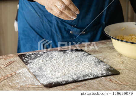 Chef dusting flour over a dark surface to prepare dough, emphasizing traditional culinary craft, artisanal baking processes, and the authentic creation of homemade bread in a rustic kitchen Chef dusting flour over a dark surface to prepare dough, emphasizing traditional culinary craft, artisanal baking processes, and the authentic creation of homemade bread in a rustic kitchen 139639079