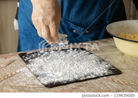 An elderly person carefully dusts flour over a dark surface to prepare fresh dough for baking bread, capturing authentic traditional culinary methods and the true joy of homemade kitchen cooking 139639080