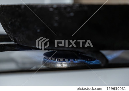 Cast iron frying pan resting on a gas stove burner with blue flame, representing home cooking, preparation of healthy food, professional culinary art, and sustainable lifestyle daily routine Cast iron frying pan resting on a gas stove burner with blue flame, representing home cooking, preparation of healthy food, professional culinary art, and sustainable lifestyle daily routine 139639081