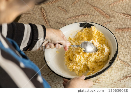 A person stirs a yellow cottage cheese mixture in a rustic bowl with a spoon for homemade cooking, representing traditional food preparation techniques and an authentic home culinary lifestyle 139639088
