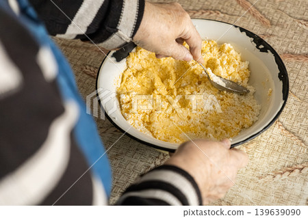 An elderly person stirs fresh dough in a metal bowl, highlighting traditional homemade culinary craft and healthy nutrition as key parts of a sustainable lifestyle in a warm home kitchen An elderly person stirs fresh dough in a metal bowl, highlighting traditional homemade culinary craft and healthy nutrition as key parts of a sustainable lifestyle in a warm home kitchen 139639090