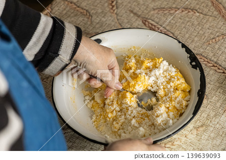 Person mixing fresh cottage cheese and raw egg yolk in a bowl, preparing traditional homemade pastry dough for baking to emphasize culinary skills and authentic farmhouse kitchen cooking Person mixing fresh cottage cheese and raw egg yolk in a bowl, preparing traditional homemade pastry dough for baking to emphasize culinary skills and authentic farmhouse kitchen cooking 139639093