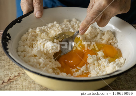 An elderly person carefully mixes fresh raw eggs and creamy cottage cheese in a rustic kitchen bowl, demonstrating traditional methods for preparing healthy and protein rich home meals An elderly person carefully mixes fresh raw eggs and creamy cottage cheese in a rustic kitchen bowl, demonstrating traditional methods for preparing healthy and protein rich home meals 139639099