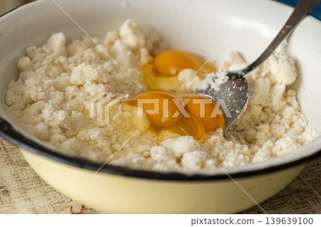 Fresh eggs combined with soft cottage cheese in a ceramic mixing bowl, preparing healthy ingredients for traditional homemade pastry or morning breakfast recipes in a bright kitchen setting 139639100