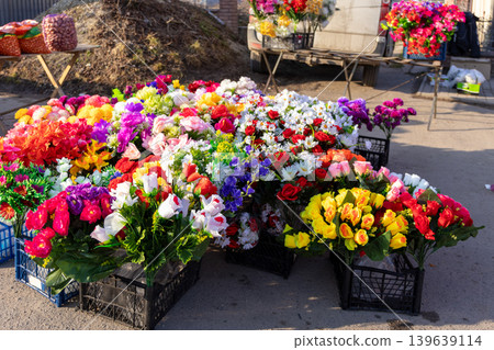 Colorful artificial flower bouquets are neatly arranged in plastic crates at an outdoor market stall, highlighting seasonal decor and floral arrangements for graveside memory tributes Colorful artificial flower bouquets are neatly arranged in plastic crates at an outdoor market stall, highlighting seasonal decor and floral arrangements for graveside memory tributes 139639114