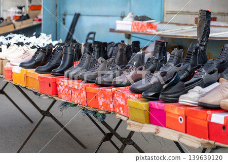 A wide variety of leather footwear is neatly displayed on colorful shoe boxes at an outdoor market stall, highlighting diverse retail styles and seasonal fashion trends for local shoppers A wide variety of leather footwear is neatly displayed on colorful shoe boxes at an outdoor market stall, highlighting diverse retail styles and seasonal fashion trends for local shoppers 139639120