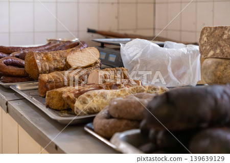 Assortment of smoked meat products displayed on trays in a professional butchery, representing traditional artisanal food preparation, rustic culinary heritage and premium deli stock selection Assortment of smoked meat products displayed on trays in a professional butchery, representing traditional artisanal food preparation, rustic culinary heritage and premium deli stock selection 139639129