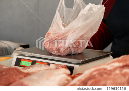 Raw meat in plastic bag being weighed on digital scale at butcher shop counter for purchase, highlighting food retail service and market industry quality control standards in local business Raw meat in plastic bag being weighed on digital scale at butcher shop counter for purchase, highlighting food retail service and market industry quality control standards in local business 139639136