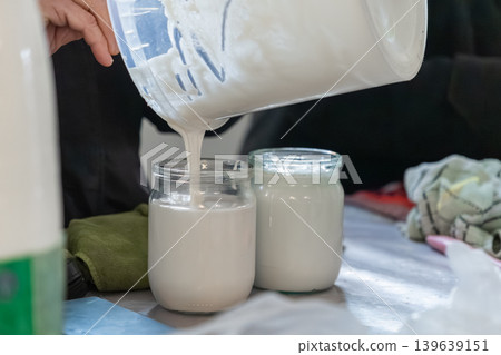 A person pours fresh, thick sour cream into a glass jar, demonstrating an artisanal dairy production process in a clean kitchen to represent healthy, organic, and homemade food nutrition 139639151