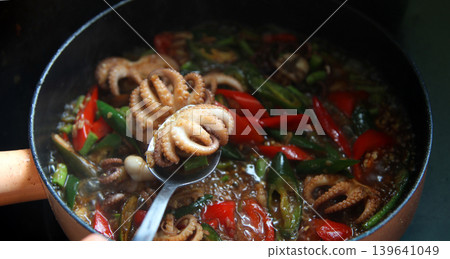 cooking spicy stir-fried baby octopus with basil and chili in a hot pan with steam, high-angle view of delicious Asian seafood cuisine cooking spicy stir-fried baby octopus with basil and chili in a hot pan with steam, high-angle view of delicious Asian seafood cuisine 139641049