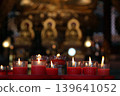 Red candles burning in glass cups on a prayer altar, with a blurred golden Buddha statue in the background. A symbol of faith, peace, and spiritual light in a Chinese temple 139641052