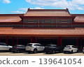 Traditional Chinese temple architecture with intricate colorful patterns and red pillars, featuring a parking lot with modern cars in Thailand. A blend of ancient culture and modern life 139641054