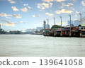 Traditional wooden houses on stilts along the Chao Phraya River in Bangkok, Thailand, with a modern city skyline and bright blue sky background, representing old and new lifestyle 139641058