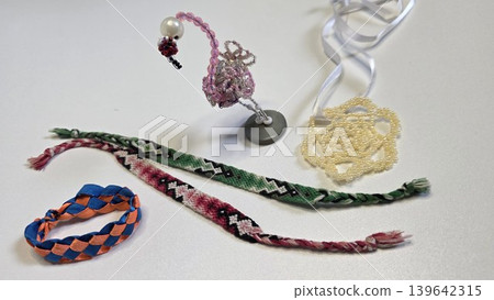 Handmade beaded pink flamingo toy and woven friendship bracelets scattered against seamless white background, concept of creative kids craft and hobby Handmade beaded pink flamingo toy and woven friendship bracelets scattered against seamless white background, concept of creative kids craft and hobby 139642315