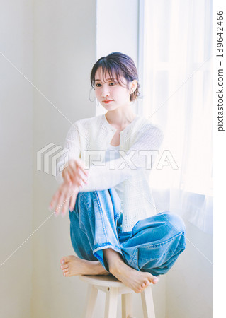 一位穿著牛仔褲的年輕女子坐在椅子上。 一位穿著牛仔褲的年輕女子坐在椅子上。 139642466