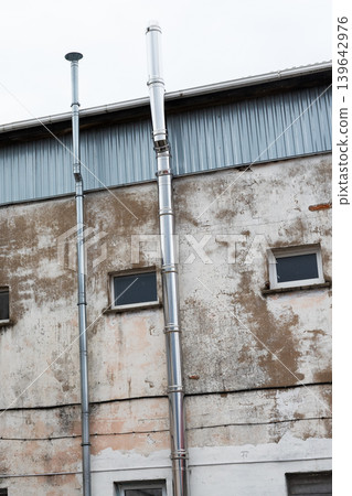 Old industrial building showing deterioration. Weathered factory wall with peeling paint and vents 139642976