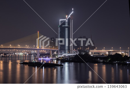 A modern skyscraper and an illuminated suspension bridge the golden Thotsamarachan Bridge (Rama IX Bridge) the night sky, mirroring their brilliant lights across the dark, undulating surface of the A modern skyscraper and an illuminated suspension bridge the golden Thotsamarachan Bridge (Rama IX Bridge) the night sky, mirroring their brilliant lights across the dark, undulating surface of the 139643063
