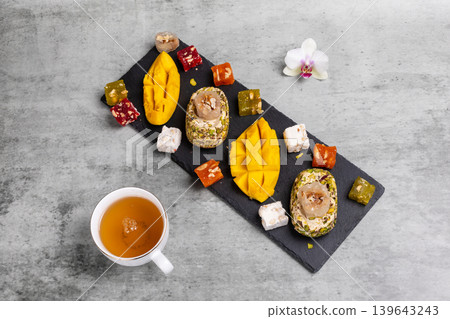 Cup of tea. Halva, fresh mango and fruit sweets with nuts on the cutting board. Cup of tea. Halva, fresh mango and fruit sweets with nuts on the cutting board. 139643243
