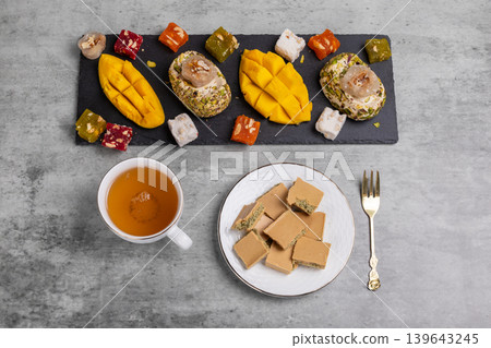 Cup of tea. Plate with chocolate. Halva, fresh mango and fruit sweets with nuts on the cutting board. Cup of tea. Plate with chocolate. Halva, fresh mango and fruit sweets with nuts on the cutting board. 139643245