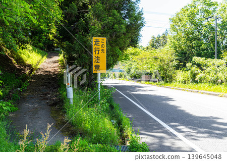 一塊「小心駕駛」的標誌牌和一條綠樹環繞的道路。 一塊「小心駕駛」的標誌牌和一條綠樹環繞的道路。 139645048