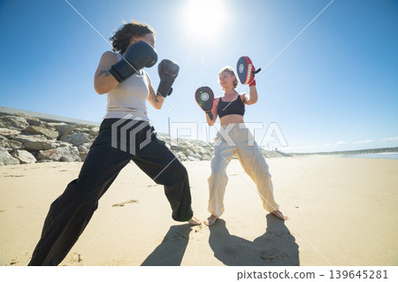 Women training boxing on beach with focus mitts Women training boxing on beach with focus mitts 139645281