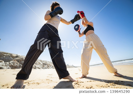 Women boxing training on sunny beach with focus mitts Women boxing training on sunny beach with focus mitts 139645290