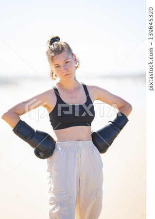 Determined young woman wearing boxing gloves posing outdoors Determined young woman wearing boxing gloves posing outdoors 139645320